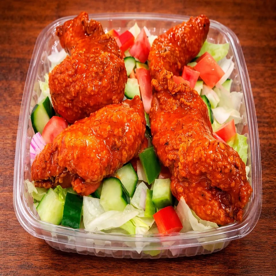 Four buffalo chicken wings on a bed of fresh lettuce, cucumbers, and tomatoes in a plastic container.