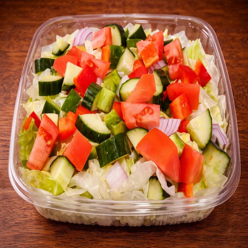 Fresh garden salad with lettuce, tomatoes, cucumbers, and red onions in a clear plastic container.